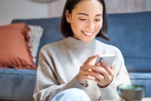 Technology and people. Young stylish asian woman sits at home with her smartphone, texting message